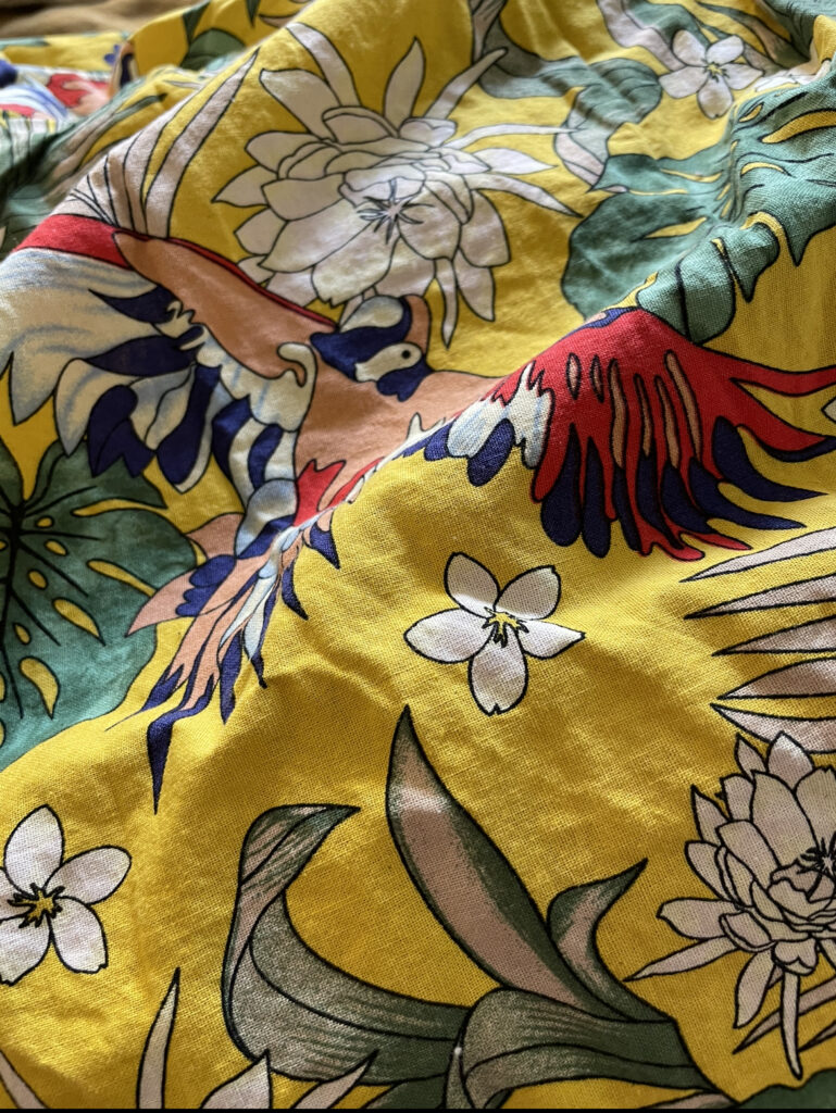 a swatch of vibrant yellow linen with vibrant tropical flowers and foliage and red and blue birds